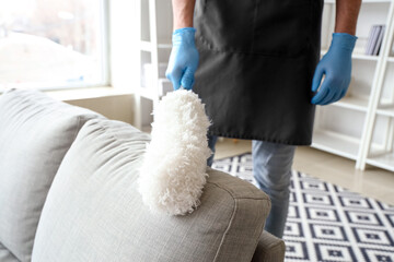 Male janitor cleaning sofa with pp-duster in living room, closeup