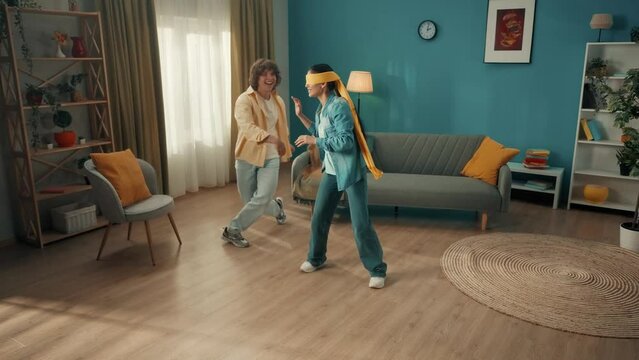 A young married couple spends time together, having fun. A couple is playing a game of blind man's buff. A blindfolded Asian woman catches a man dodging her. Family relax and entertainment at home.