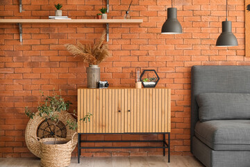 Wooden cabinet with florarium, photo camera and pampas grass near brick wall