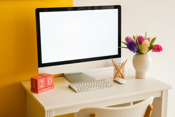 Modern PC, mouse, keyboard, calendar, pencils and hyacinth flowers on table near color wall