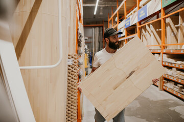 A young handsome man with a beard in casual clothes in a construction hypermarket in the lumber department selects wood building materials for the renovation of his house.
