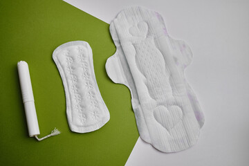 Women's pads and tampon. Sanitary pads lie next to a tampon on an isolated background on a green and white background. The concept of health, feminine hygiene and the menstrual cycle
 - obrazy, fototapety, plakaty