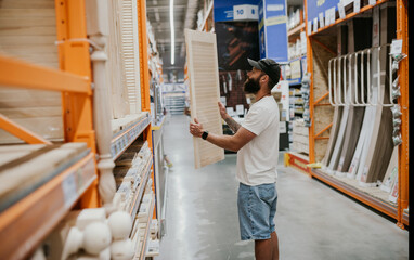 A young handsome man with a beard in casual clothes in a construction hypermarket in the lumber...