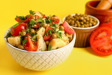 Bowl of tasty Potato Salad with vegetables on yellow background