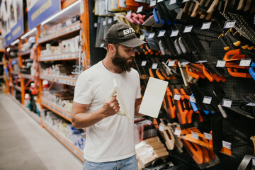 Young handsome man with a beard in casual clothes in a construction hypermarket chooses tools