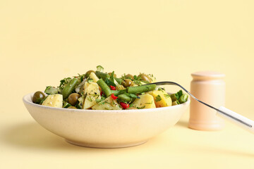 Bowl of tasty Potato Salad with vegetables on yellow background