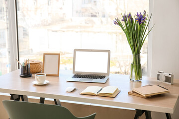 Modern workplace with laptop, notebooks, coffee cup and flowers in office