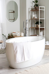 Interior of light bathroom with bathtub, mirror and shelving unit