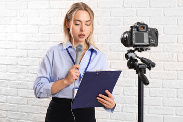 Female journalist with microphone and clipboard recording video on white brick background