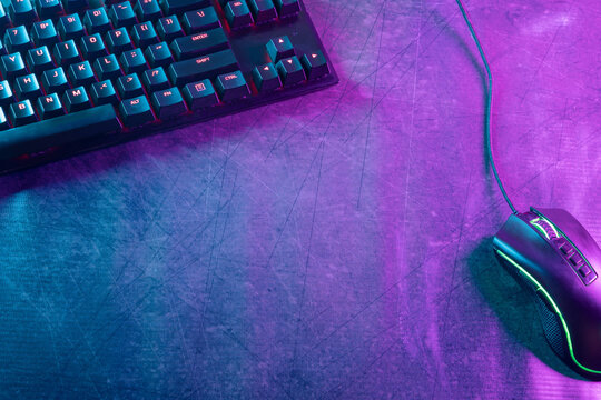 Top view with ample copy space of a gaming-themed desktop adorned with professional gaming accessories, illuminated by vibrant cyberpunk neon lights. - Powered by Adobe