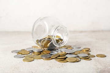 Overturned jar with coins in beige grunge table. Savings concept