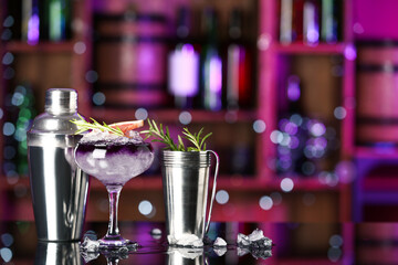 Glass of purple gin and tonic with bartender equipment, grapefruit and rosemary on table in bar...