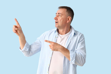 Shocked mature man pointing at something on blue background