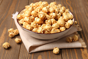 Bowl with crispy popcorn on wooden background