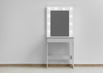 Modern white makeup dressing table with mirror and backlight on a white wall close-up.