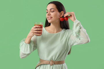 Young woman with glass of vegetable juice and tomatoes on green background