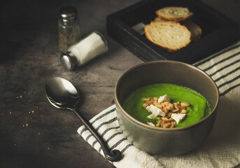 Closeup shot of spinach soup garnished with almonds in a gray bowl on the table