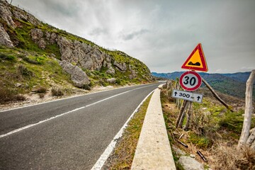 Road sign with a speed limit of 30 km per hour near a rocky hillside and under a cloudy sky