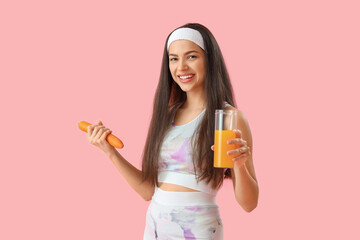 Sporty young woman with glass of vegetable juice and carrot on pink background