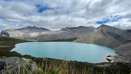 Beautiful view of a small blue lake surrounded by mountains under a cloudy sky.