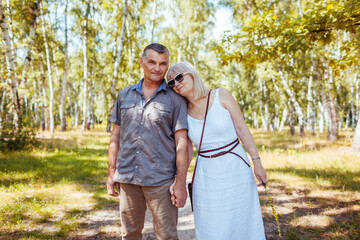 Portrait of senior family couple walking outdoors in summer forest. Elderly people holding hands and hugging.