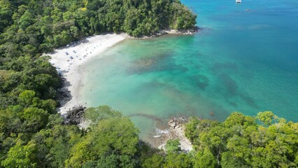 Obraz premium Aerial shot above a beach surrounded by tropical trees in front of an azure sea