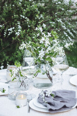 Rustic elegant eco friendly zero waste trendy wedding reception table decor with fresh spring apple cherry flowers in bloom. Beautiful marriage decoration, holiday event outdoors in the family garden