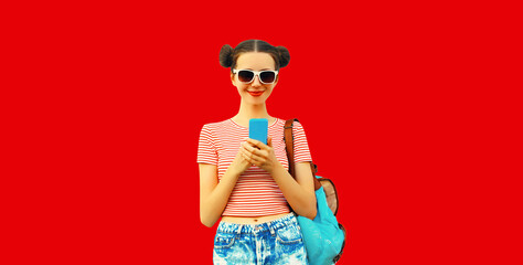 Portrait of happy smiling young woman looking at smartphone wearing backpack with cool girly hairstyle on red background