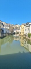 Fototapeta premium Vertical shot of the Alzette river between city buildings on a sunny day, in Luxembourg