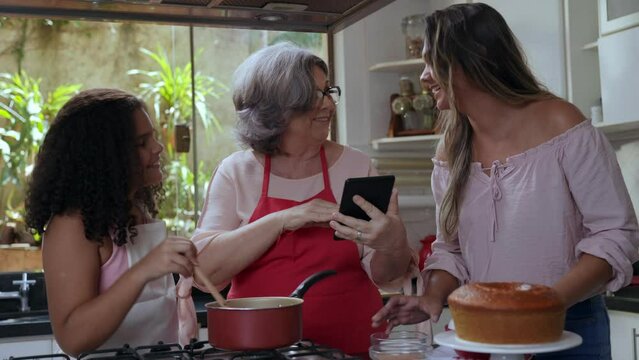 crian&ccedil;a brasileiro fazendo brigadeiro de panela para bolo na cozinha junto com sua m&atilde;e e sua av&oacute; no dia das m&atilde;es