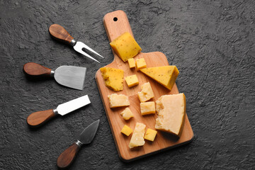 Wooden board with pieces of tasty cheese on dark background