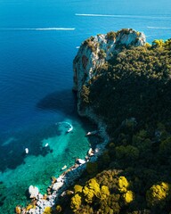 Vertical aerial shot of a cliff and tropical trees in front od a blue sea in Capri, Italy - obrazy, fototapety, plakaty
