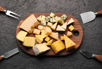 Wooden board with pieces of tasty cheese on dark background