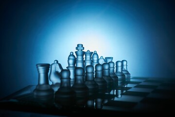 Chess board and transparent chess figures with blue and black background in close up.