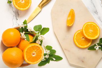 Board and bowl of oranges with blooming branches on white table
