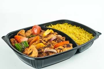 Rice and roasted meat and vegetables in a black container against white background
