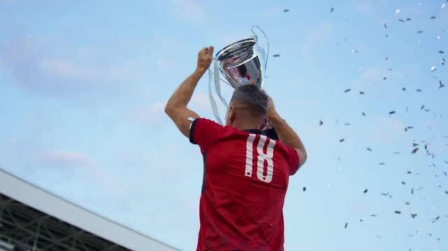 Portrait of Caucasian male soccer football player celebrating victory in the championship, lifting the trophy above his head in a huge stadium. Super slow motion shot