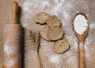 Bread slices and a spoon with flour on brown surface