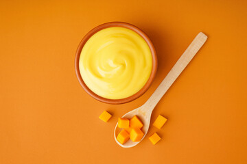 Bowl of tasty cheddar sauce and spoon with cheese cubes on orange background