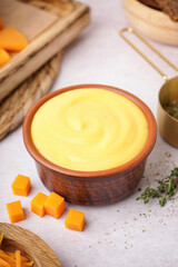 Bowl with tasty cheddar cheese sauce and measuring cup of rosemary on white grunge background