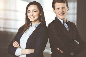 Friendly young colleagues are standing as a team with crossed arms in sunny office. Successful business people at work.