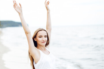 Fototapeta na wymiar Happy smiling woman in free happiness bliss on ocean beach standing with raising hands. Portrait of a multicultural female model in white summer dress enjoying nature during travel holidays vacation o
