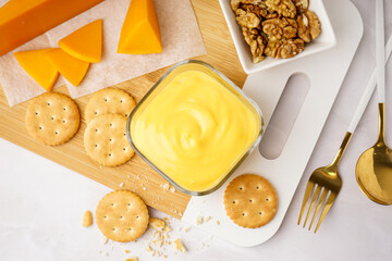 Bowls of tasty cheddar sauce with crackers, cheese chunks and walnuts on white grunge background
