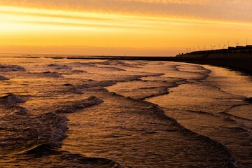 Aerial shot of layered waves of a sea washing the coast at a golden sunset