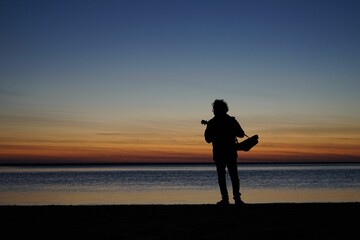 Fototapeta na wymiar Silhouette of male playing thukulele in front of sea during sunset