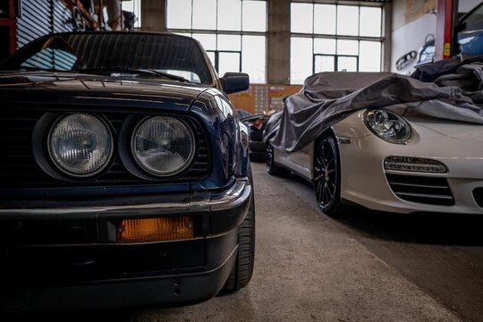 Blue BMW and a white 911 Porsche with a shower cap parked in a garage