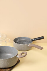 Cooking pots and whisk on beige background