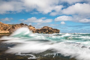 Beautiful shot of sea waves crashing on a beach surrounded by cliffs
