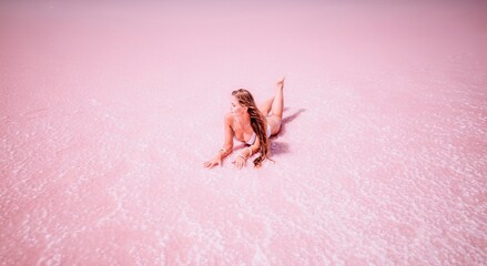 Woman in a pink salt lake. She lies in a white bathing suit. Wanderlust photo for memory