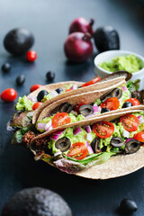 A healthy lunch or dinner of a vegan  vegetarian soft shell taco wrap made with red quinoa with taco season, romaine lettuce, sliced tomatoes, guacamole, black olives and red onions. Selective focus. - obrazy, fototapety, plakaty